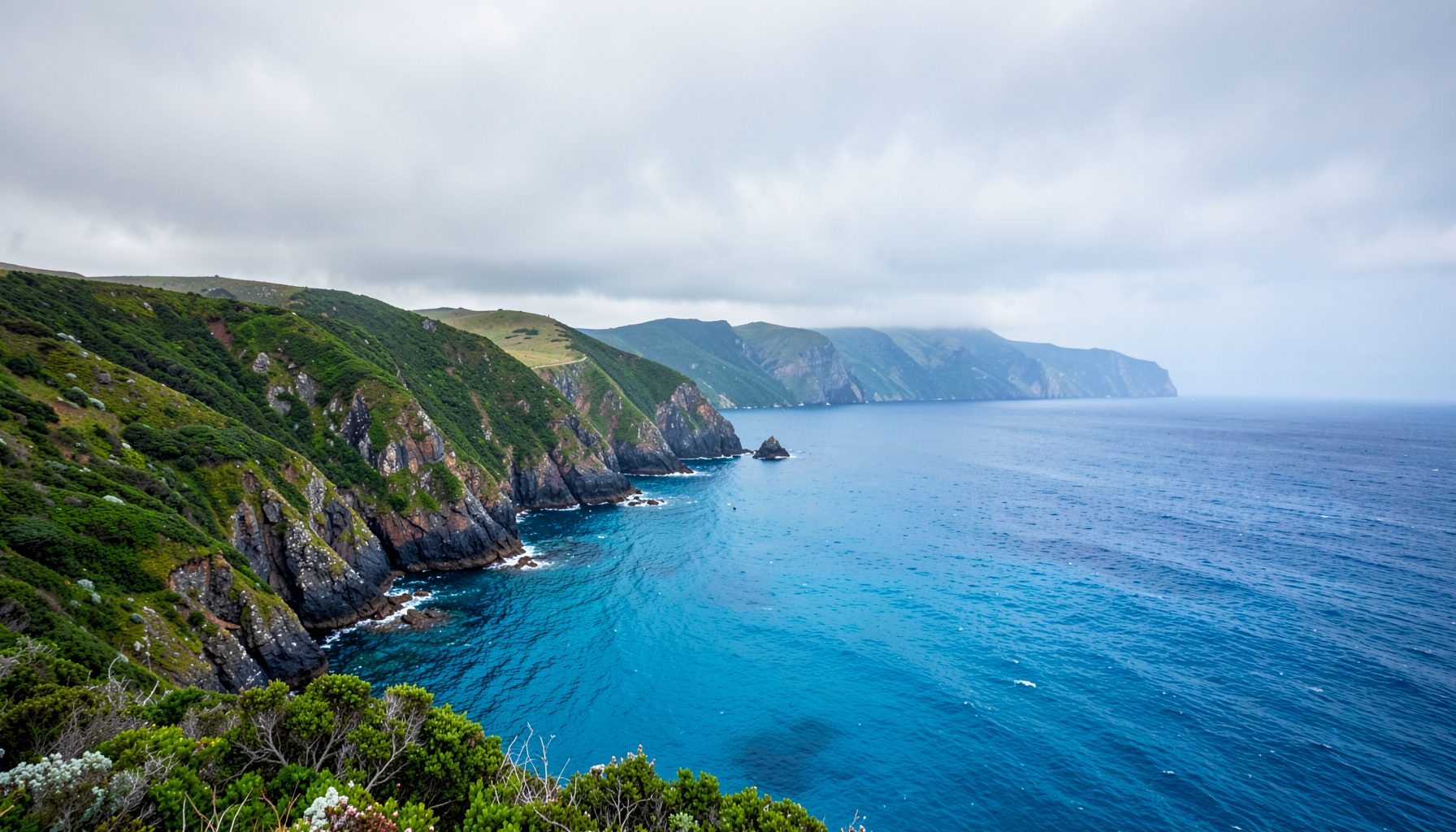 Costa vasca con acantilados verdes y mar azul intenso bajo un cielo nublado, atmósfera atlántica