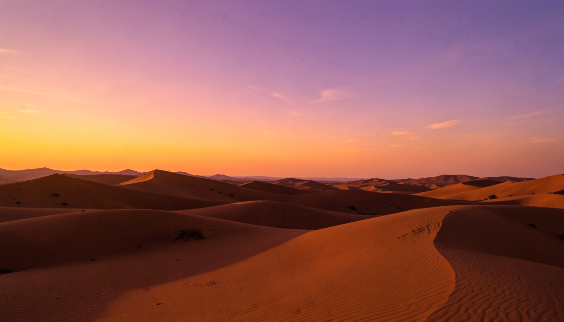Desierto marroquí con dunas doradas al atardecer, sombras alargadas y cielo en tonos naranja y violeta