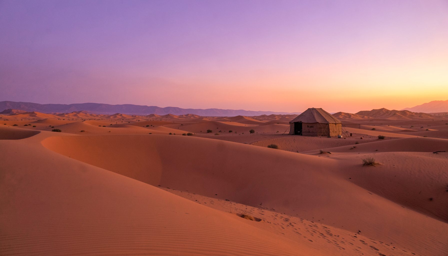 Dunas doradas del desierto de Erg Chigaga al atardecer, tienda bereber en la lejanía y cielo en tonos violeta y naranja