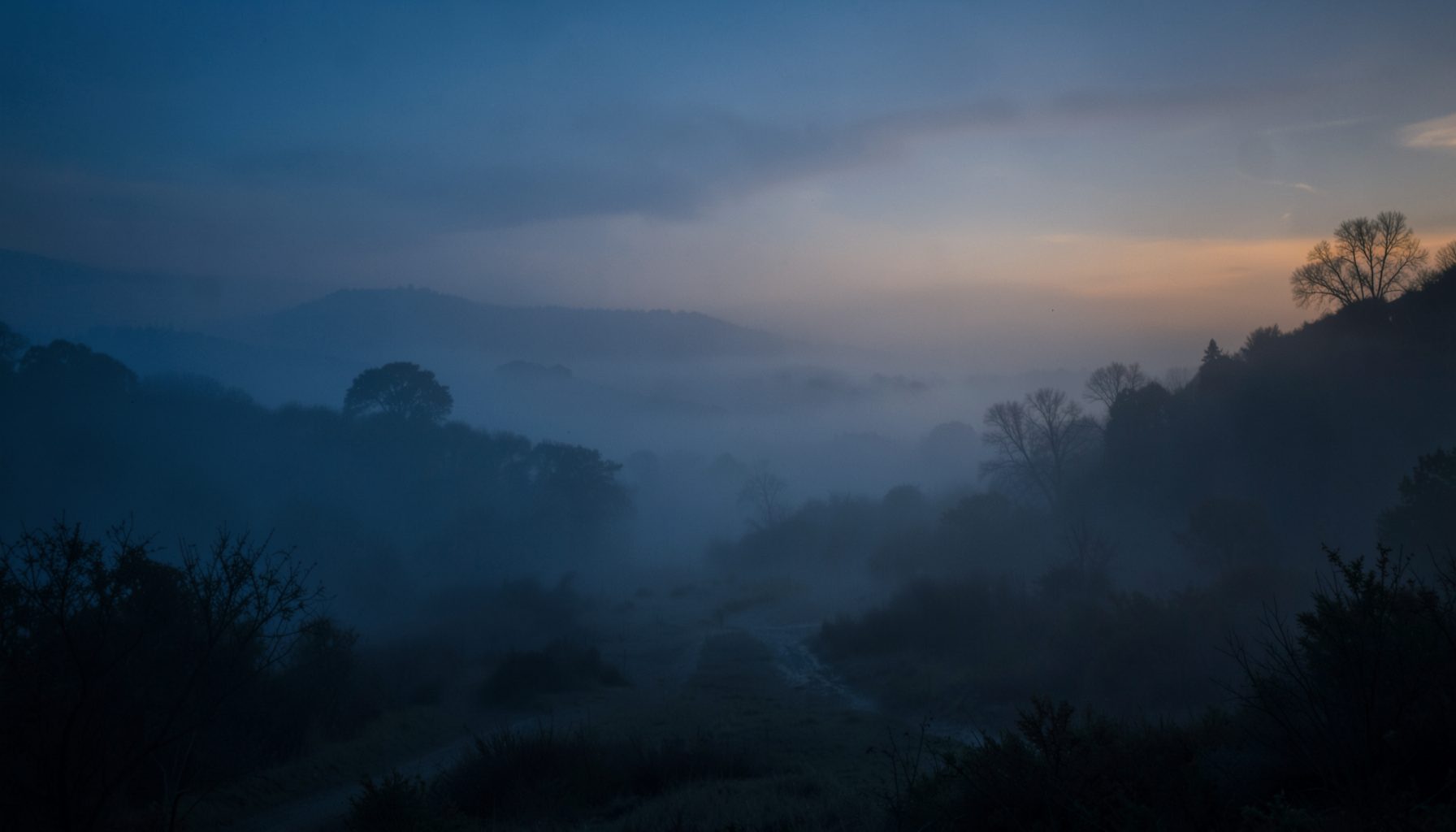 Paisaje brumoso al amanecer con tonos azules profundos y dorados suaves, transmitiendo calma y contemplación