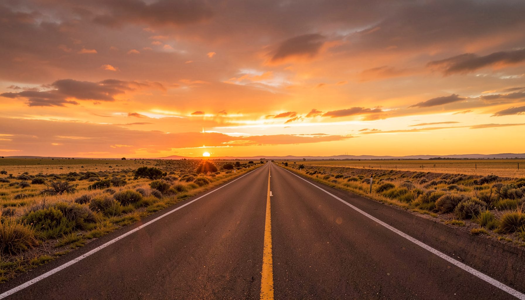Carretera abierta al atardecer con tonos dorados y naranjas, cielo amplio y sensación de libertad viajera