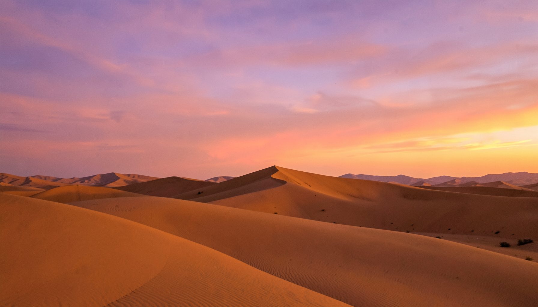 Paisaje desértico al atardecer con dunas doradas y cielo en tonos naranjas y violetas, atmósfera serena y viajera