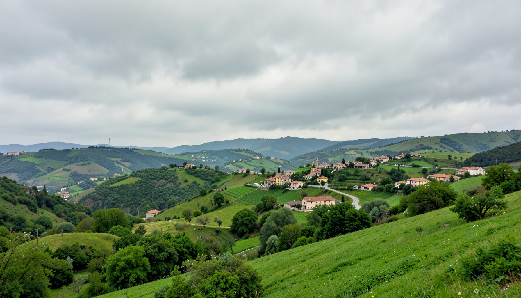 Paisaje verde de colinas y caseríos vascos bajo un cielo nublado con tonos suaves de gris y verde